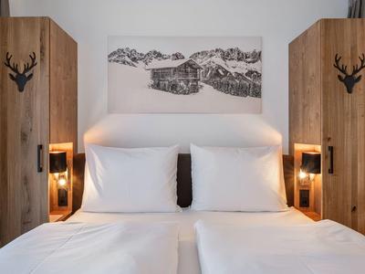 Doppelbett mit weißen Kissen und Bettwäsche, zwei Holzschränke und Bergbild an weißer Wand.