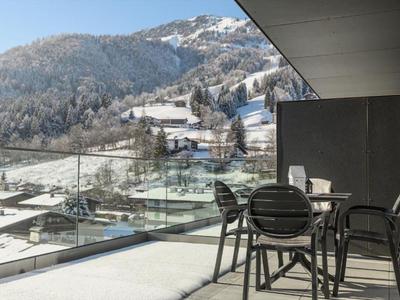 Balkon mit Stühlen und Tisch mit Blick auf verschneite Berge und Häuser.