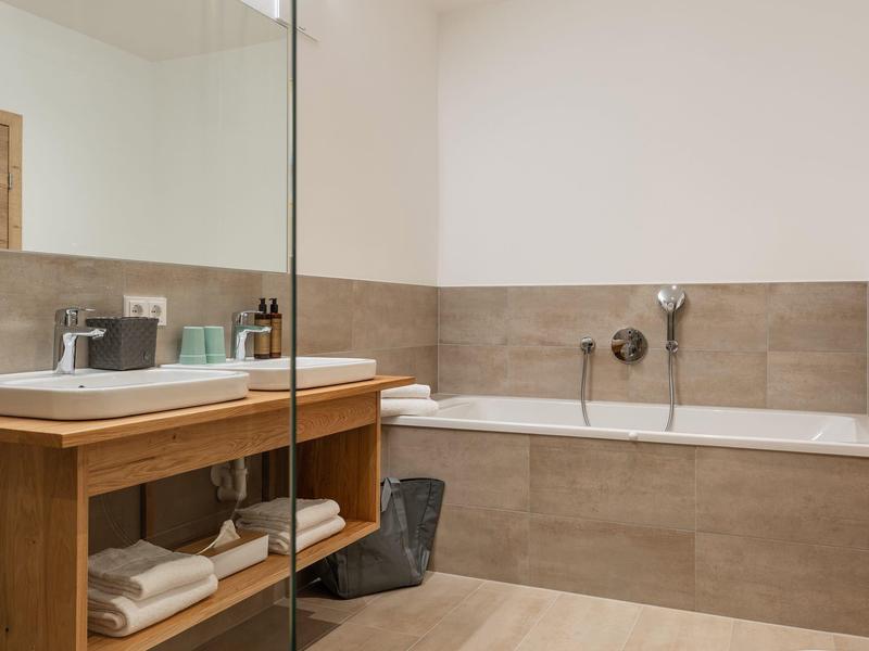 Modernes Badezimmer mit Badewanne, großem Spiegel, Holzmöbel und hellbraunen Fliesen.