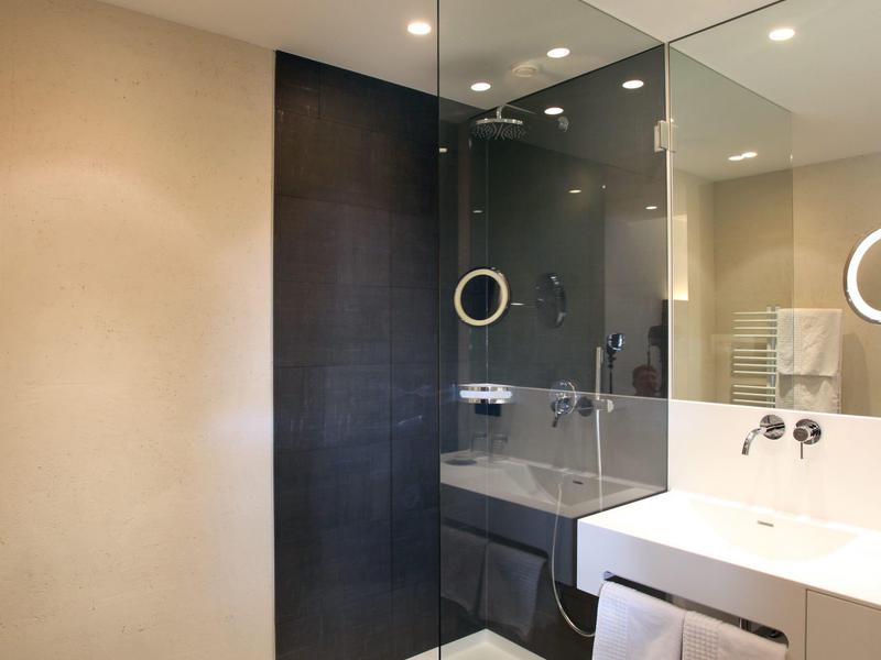 Modernes Badezimmer mit Glasdusche, schwarz-beigen Fliesen und weißem Waschbecken mit Handtüchern.