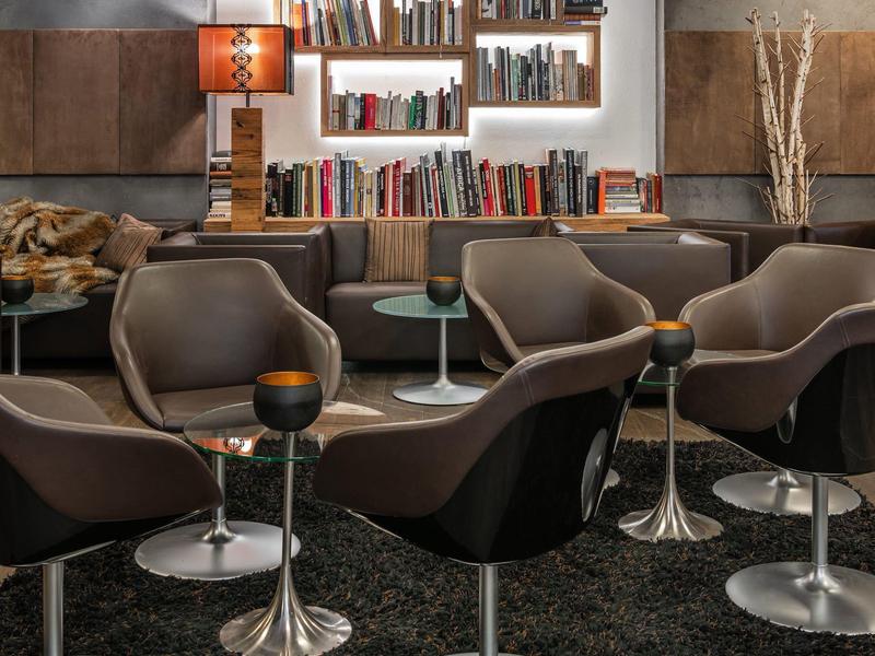 Moderner Wohnraum mit braunen Sesseln, Bücherregal, Stehlampe und dunklem Teppichboden.