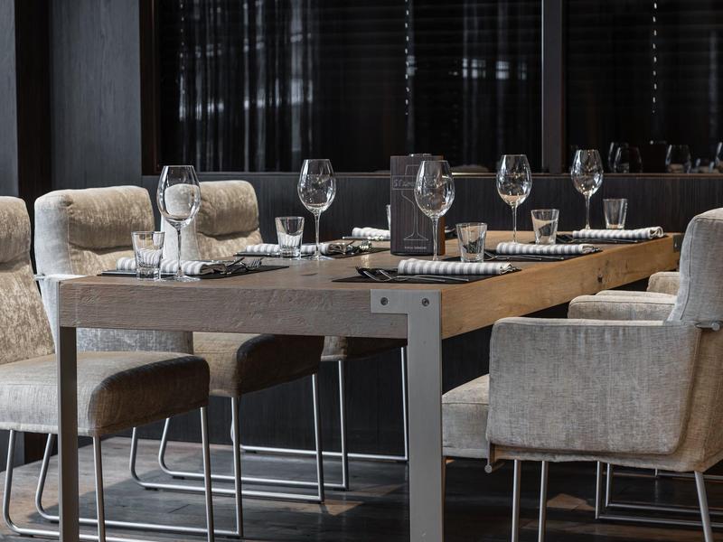 Moderner Esstisch mit beigen gepolsterten Stühlen und gedecktem Tisch in dunklem Raum.