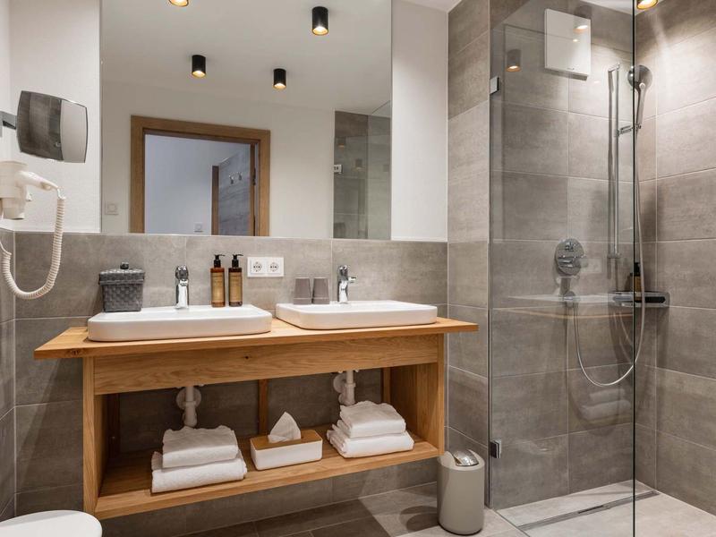 Modernes Badezimmer mit Holzwaschtisch, großen Spiegeln, grauen Fliesen und Glas-Dusche.