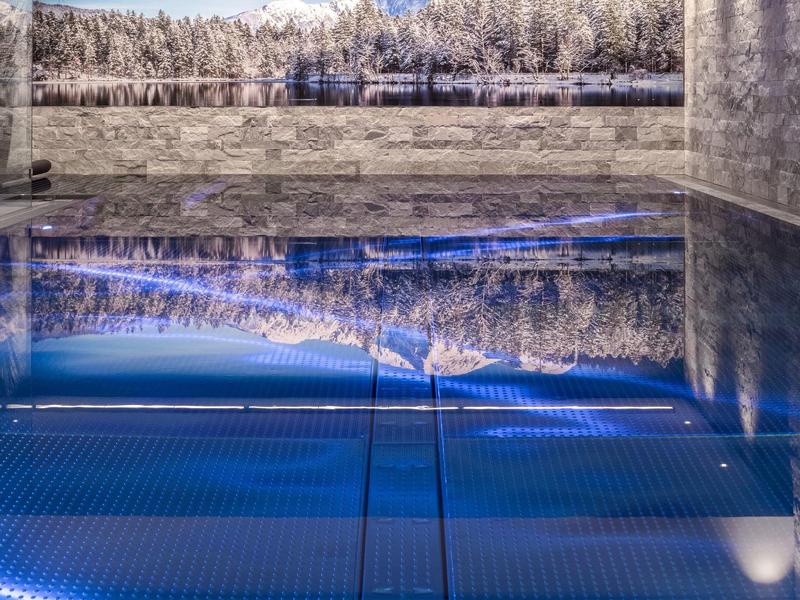 Moderner Innenpool mit spiegelnder Wasseroberfläche, beleuchtet und mit Landschaftsfoto an der Wand.