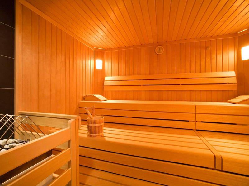 Sauna mit heller Holzverkleidung, mehrstufigen Sitzbänken und Saunaofen mit Steinen.