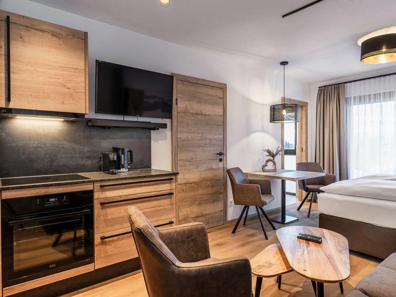 Modernes Hotelzimmer mit Holzmöbeln, Sitzbereich, Bett und großem Fenster mit Vorhängen.