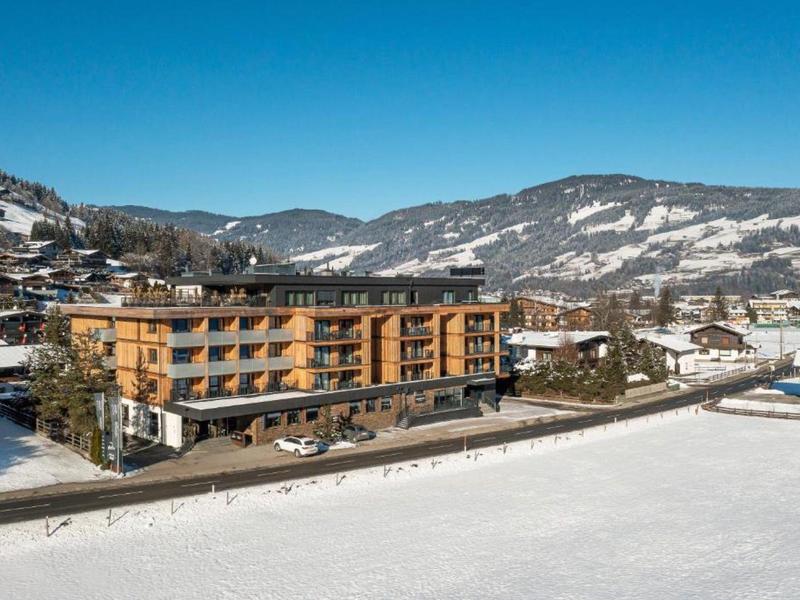 Modernes Hotelgebäude in bergiger Winterlandschaft mit schneebedecktem Boden und klarem Himmel.