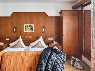 Gemütliches Schlafzimmer mit Holzwänden, Doppelbett, Jacke auf Stuhl und Wandbild.