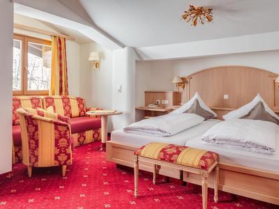 Gemütliches Hotelzimmer mit Doppelbett, rot-gelbem Sessel, Teppich und warmem Holzdekor.