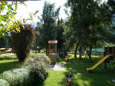 Garten mit grünem Gras, Bäumen, Sträuchern, Spielplatzgerät mit Rutsche und Schaukel.