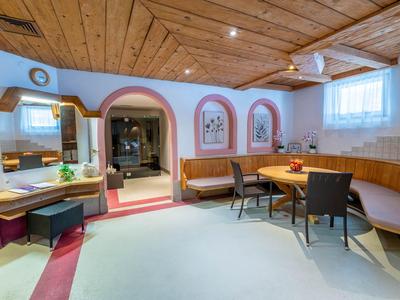 Przytulna część wypoczynkowa hotelu z drewnianym sufitem, narożną ławką i okrągłymi stołami.