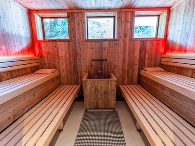 Drewniana sauna z dwoma ławkami, trzema małymi oknami i piecem pośrodku.