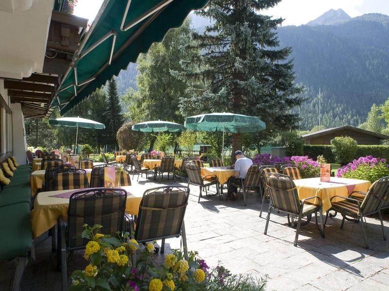 Terrassenrestaurant mit Tischen, Stühlen, Sonnenschirmen und Berglandschaft im Hintergrund.
