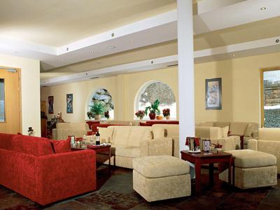 Moderner Hotel-Loungebereich mit roten und beigen Sofas, runden Tischen und Wanddekorationen.