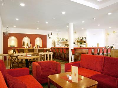 Modern eingerichteter Hotelbar- und Loungebereich mit roten Sofas und Holzmöbeln.