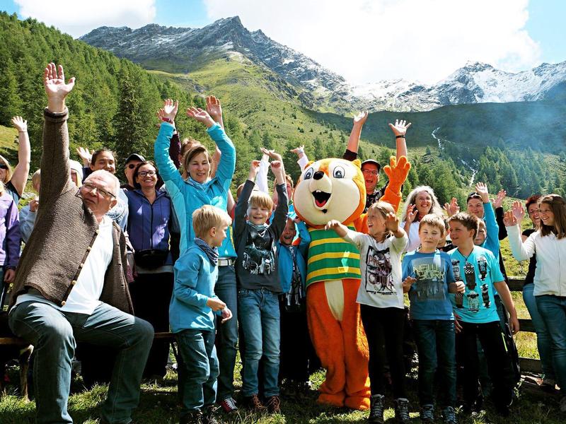 Gruppe von Menschen und Kindern mit einer verkleideten Figur vor einer Berglandschaft