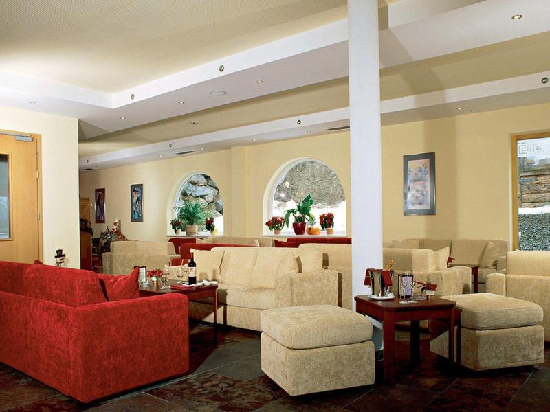 Moderner Hotel-Loungebereich mit roten und beigen Sofas, runden Tischen und Wanddekorationen.