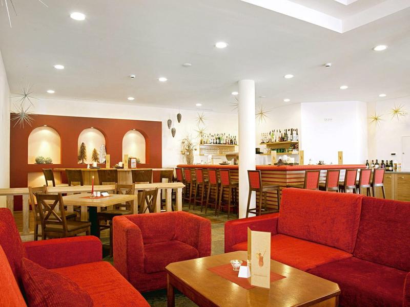 Gemütliche Hotellounge mit roten Sofas, Holztischen und freundlicher Bar im Hintergrund.