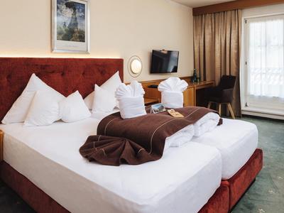 Gemütliches Hotelzimmer mit rotem Bett, braunen Decken, TV und Balkon mit Vorhängen.