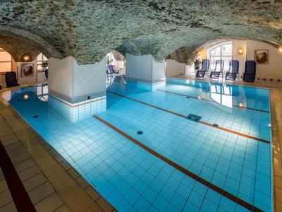 Hallenschwimmbad mit Gewölbedecke, blauen Liegestühlen und hellem blauen Wasser.