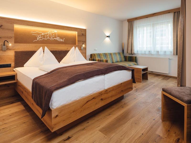 Gemütliches Hotelzimmer mit Doppelbett, Holzmöbeln und heller Fensterfront.