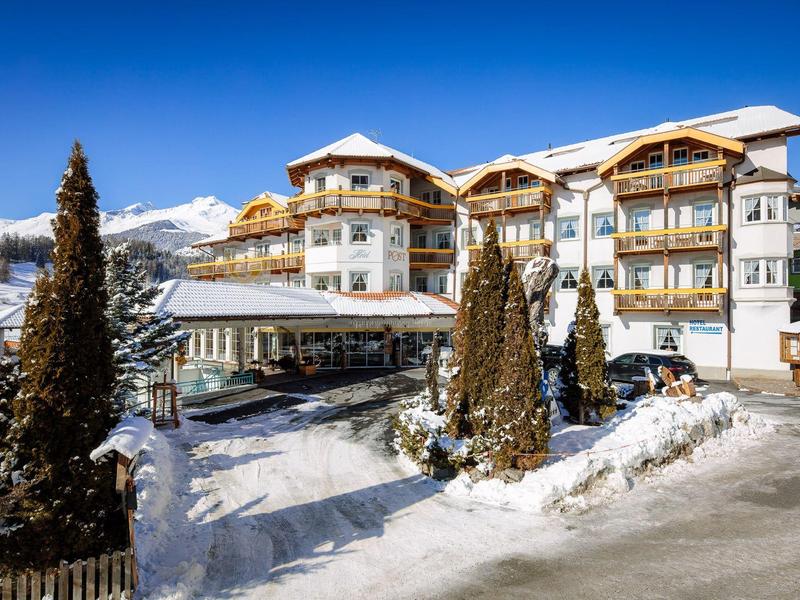 Großes Hotelgebäude in verschneiter Berglandschaft unter klarem blauem Himmel.