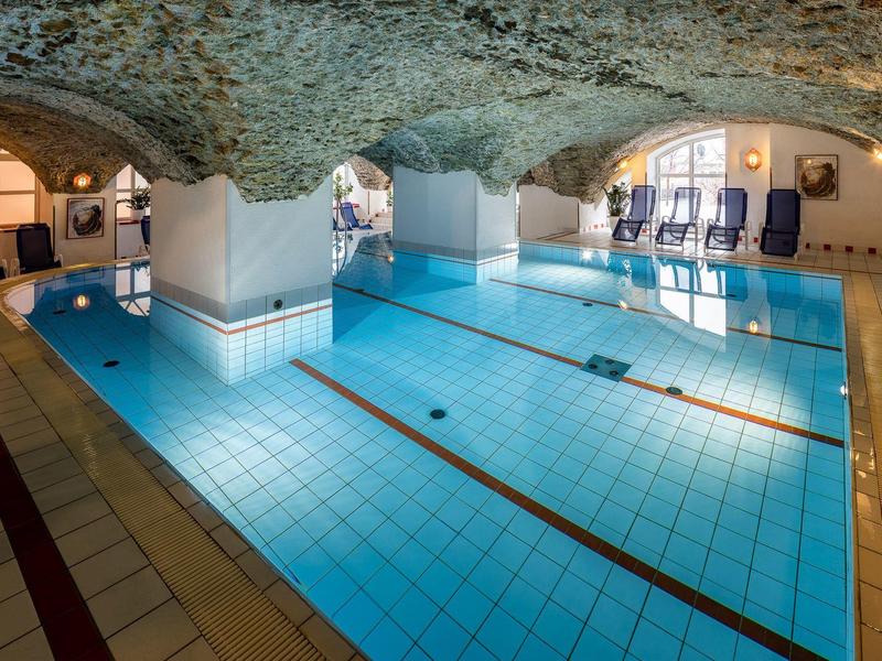 Hallenschwimmbad mit Gewölbedecke, blauen Liegestühlen und hellem blauen Wasser.