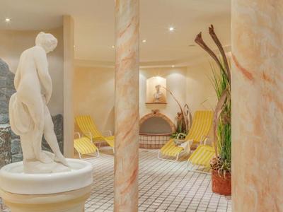 Eleganter Wellnessbereich mit Marmorstatue, entspannenden Liegestühlen und warmem Licht.