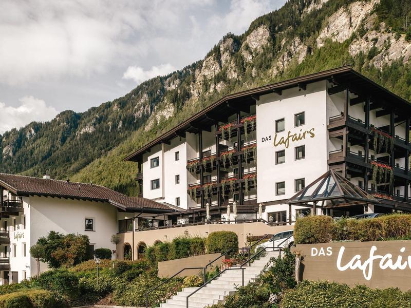 Hotelgebäude vor bewaldeten Bergen unter einem wolkigen Himmel