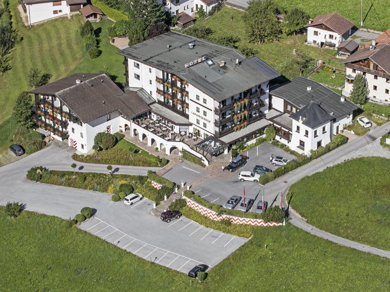Großes Hotel mit Parkplätzen umgeben von grünen Wiesen und Landhäusern.