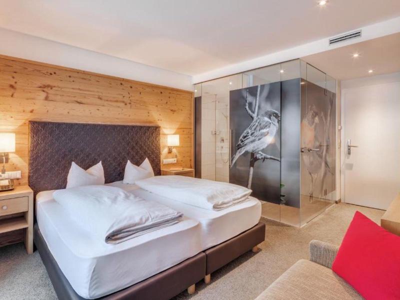 Modernes Hotelzimmer mit Doppelbett, Holzakzenten und einer Glasdusche mit Vogelmotiv.