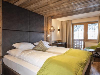 Modernes Hotelzimmer mit Holzbalkendecke, zwei Einzelbetten und großem Fenster mit Balkonblick.