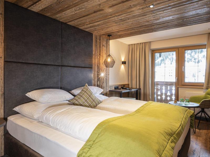 Modernes Hotelzimmer mit Holzbalkendecke, zwei Einzelbetten und großem Fenster mit Balkonblick.