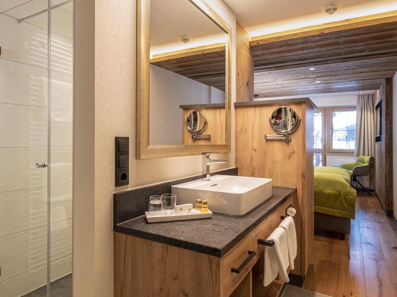 Modernes Hotelbad mit Holzdesign, eckigem Waschbecken, großer Spiegel und Blick ins Schlafzimmer.