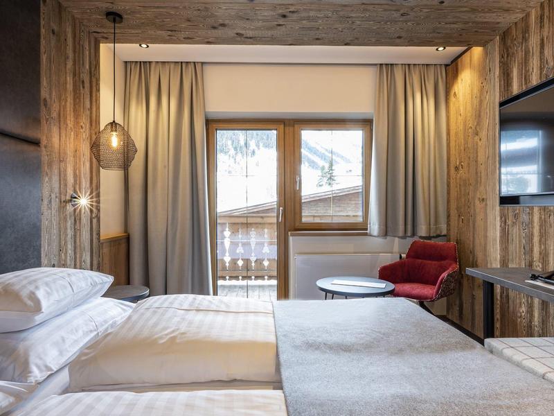 Gemütliches Hotelzimmer mit Holzvertäfelung, zwei Betten, Balkon und rotem Sessel.