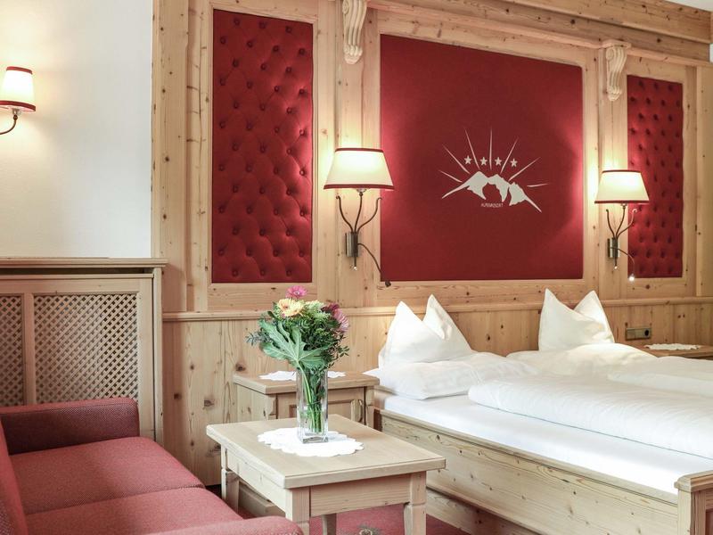 Gemütliches Hotelzimmer mit Holzvertäfelung, Doppelbett, Sofa und Tisch mit Blumen.