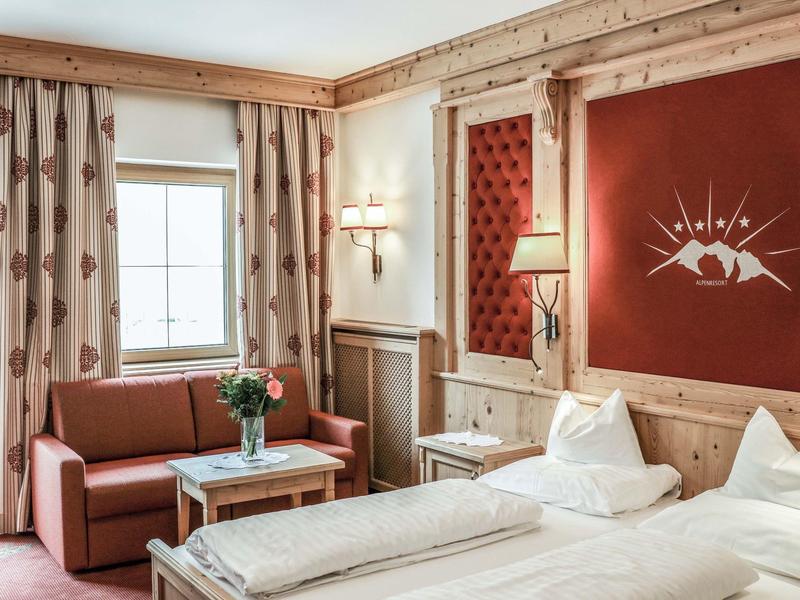 Gemütliches Hotelzimmer mit Holzmöbeln, roter Wand und komfortablem Bett neben einem Sofa