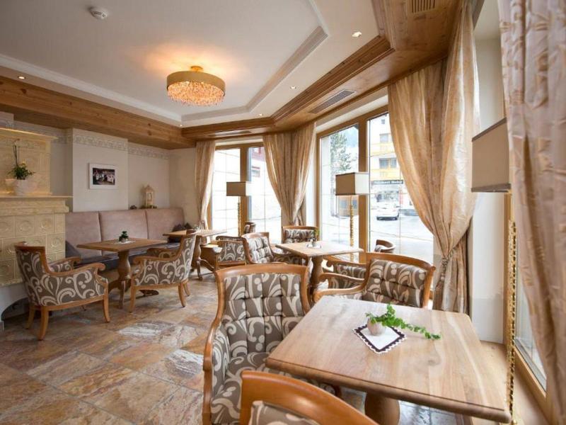 Gemütlicher Hotel-Loungebereich mit Holzstühlen, Tischen und großen Fenstern mit Vorhängen.