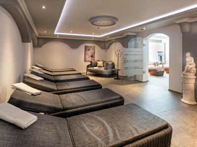 Moderner Wellnessraum mit mehreren Liegen, einer Sitzgruppe und einer dekorativen Statue.