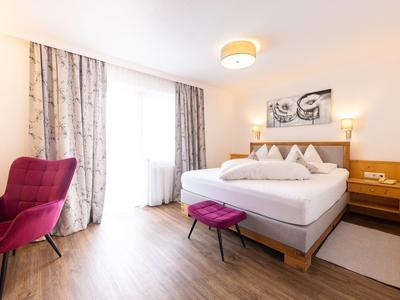 Helles Hotelzimmer mit großem Bett, violettem Stuhl und Holzboden.