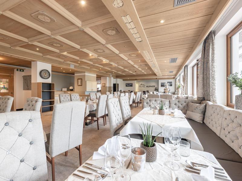 Helles Restaurant mit weißen Stühlen, gedeckten Tischen und großen Fenstern mit Blick nach draußen.