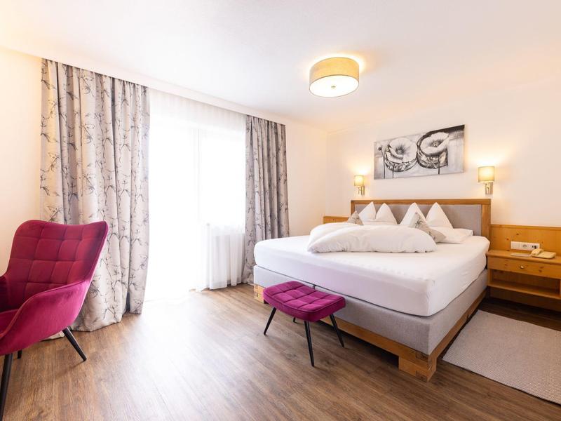 Helles Hotelzimmer mit großem Bett, violettem Stuhl und Holzboden.