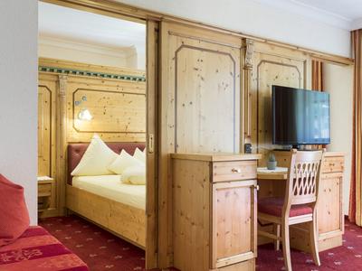 Gemütliches Hotelzimmer mit Holzmöbeln, Doppelbett, Fernseher und rotem Teppich.