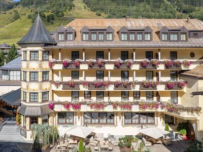 Traditionelles Hotelgebäude mit Balkonblumen und einer Türmchenstruktur in einer grünen Berglandschaft.