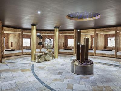 A large circular wellness room with wooden walls, seating areas, and a central fireplace.