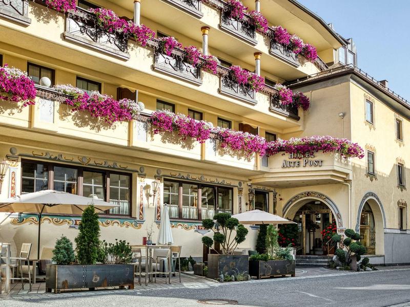Gelbes Hotel mit mehreren Stockwerken und Balkonen, verziert mit pinken Blumen in Blumenkästen.