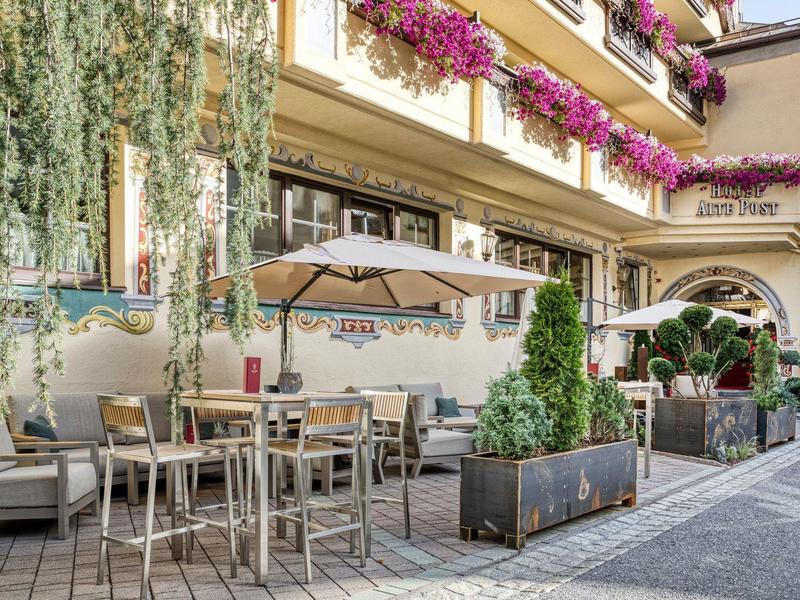 Außenbereich eines Cafés mit Tischen, Stühlen, Pflanzen und blühenden Blumen über dem Fenster.