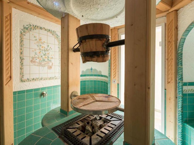 Traditioneller Holzeimer mit Schöpflöffel über einem Holzgrill in grün gefliertem Saunaraum