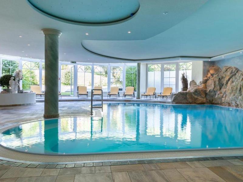 Innenpool mit Felsenwand und Panoramafenstern in einem Hotel-Spa-Bereich.