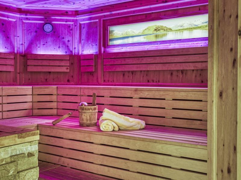 Saunaraum mit Holzbänken, Handtüchern und stimmungsvoller lila Beleuchtung